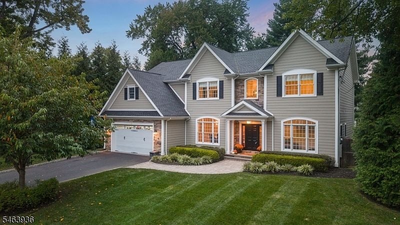 Two-story gray house with front-facing gables, a white garage door, and glowing windows at dusk.