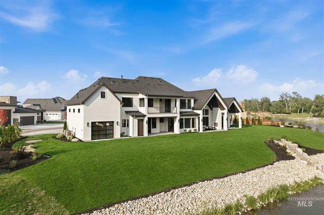 Large white two-story home beside a green lawn and rocky waterway.