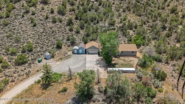 Two homes and driveways among dry, scrub-covered hillsides, seen from above.