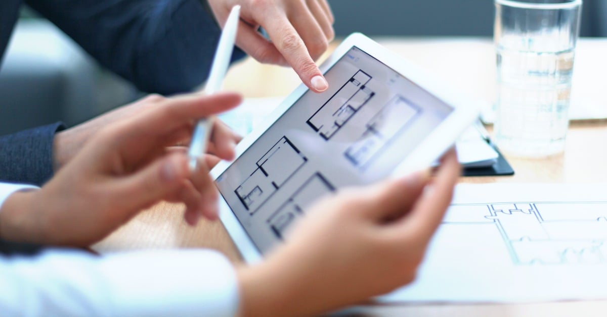 A close-up of a person holding an electronic tablet with various home floor plan options while another person points.