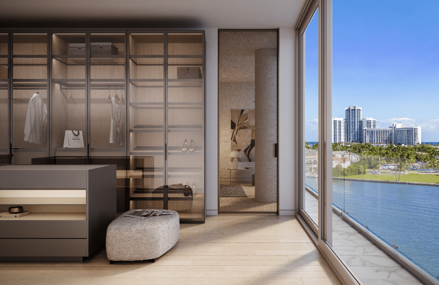 Walk-in closet with glass-front wardrobes and an ottoman overlooking the water and high-rises.