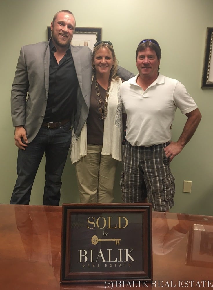 Three adults pose behind a framed Bialik Real Estate SOLD sign.