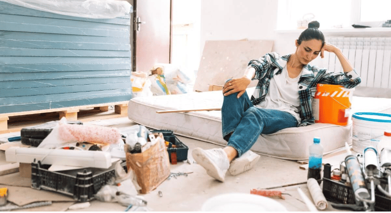 Renovation worksite with a woman seated among paint buckets, tools, and building materials.