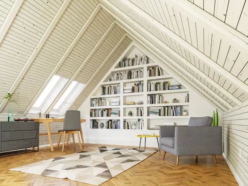 Vaulted loft sitting area with built-in bookshelves, gray chairs, skylights, and a geometric rug.
