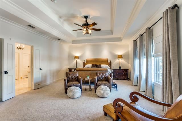 Furnished bedroom with a sitting area, tray ceiling, and large curtained windows.