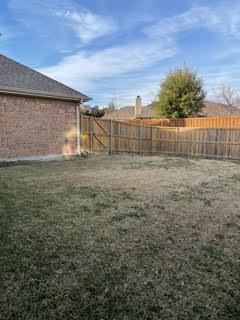 Backyard with a patchy lawn, wooden privacy fence, and tree beyond.