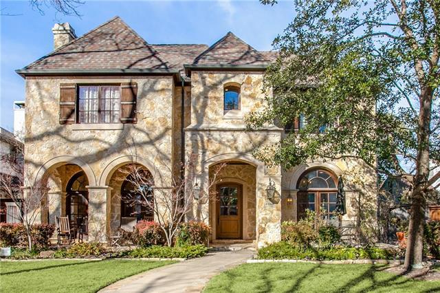 Two-story stone house with arched windows, a tiled roof, and a landscaped front lawn.