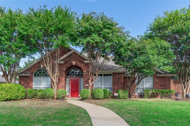 Red-brick home with a bright red door, arched windows, and mature trees framing the front yard.