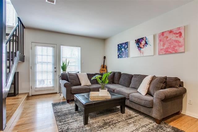 Living room with a gray sectional, patterned rug, and colorful wall art beside a staircase.