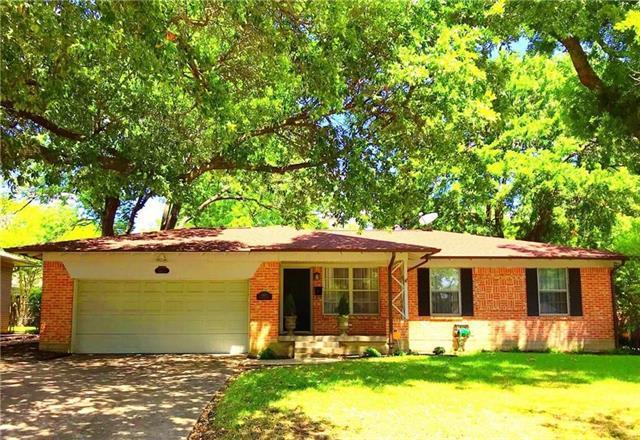 Single-story brick house with an attached garage beneath mature shade trees.