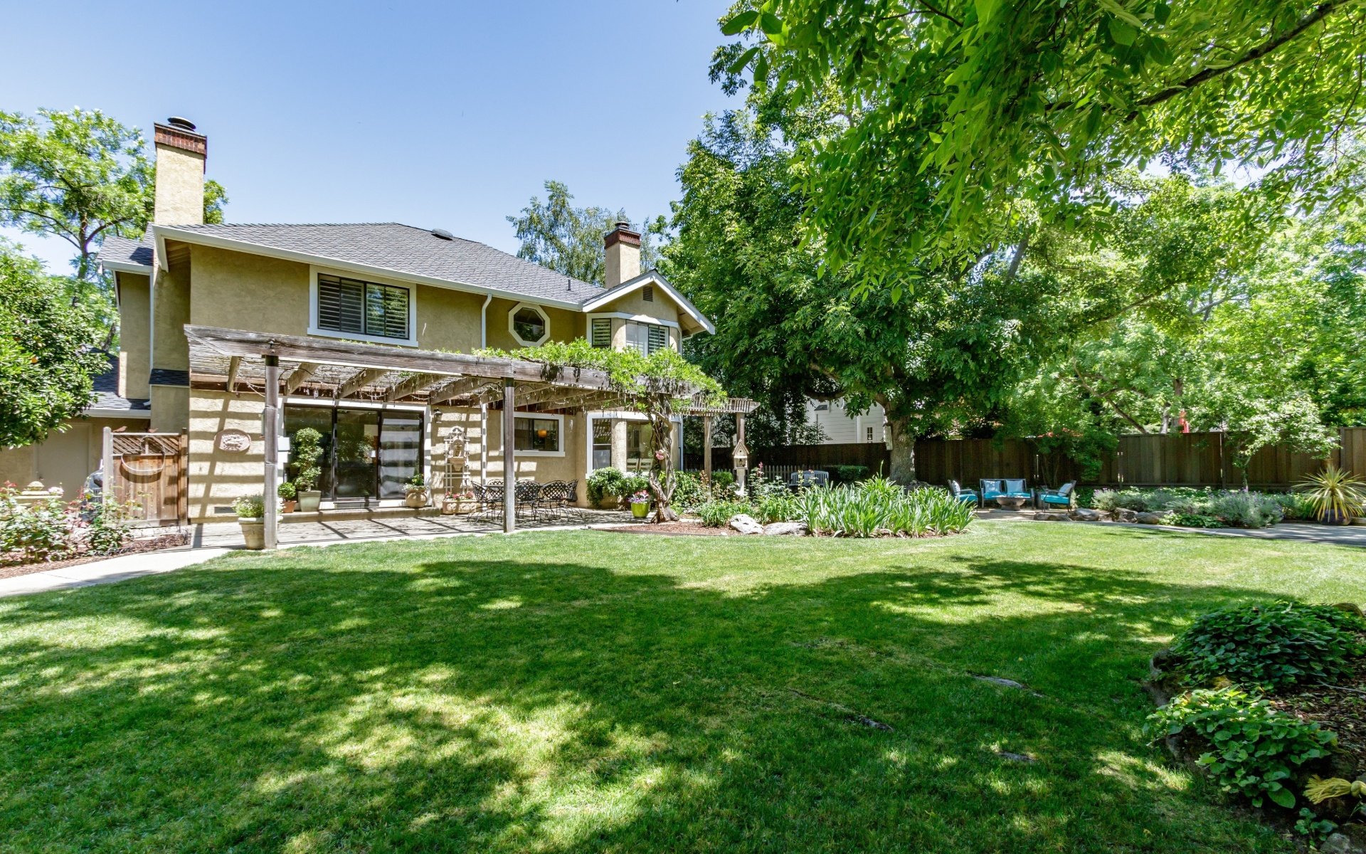 Two-story home with a pergola-covered patio, broad lawn, and mature shade trees.