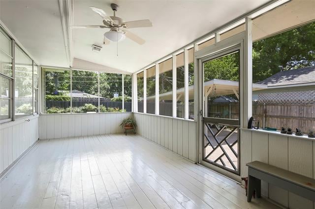 Enclosed sunroom with white plank flooring, screened windows, and a ceiling fan.