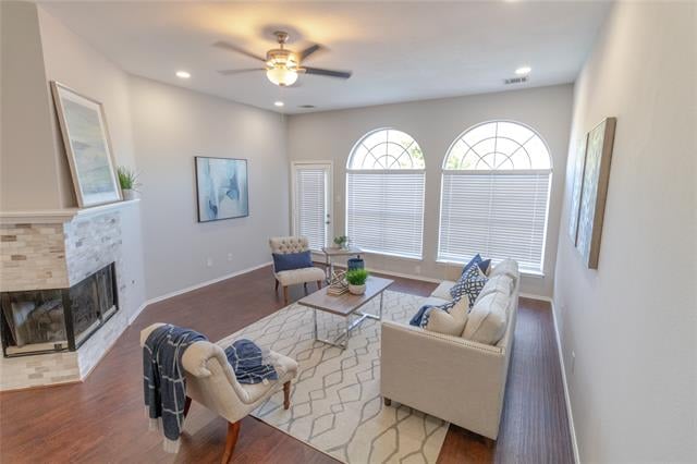 Living room with a stone fireplace, cream sofas, hardwood floors, and tall arched windows.