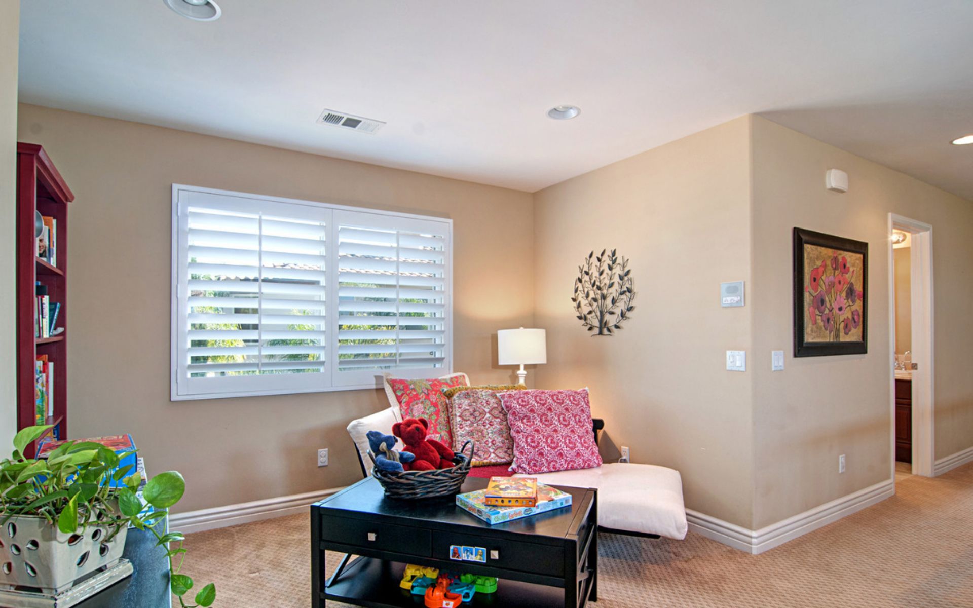 Sitting room with plantation shutters, a white sofa, colorful pillows, and toys on a black coffee table.