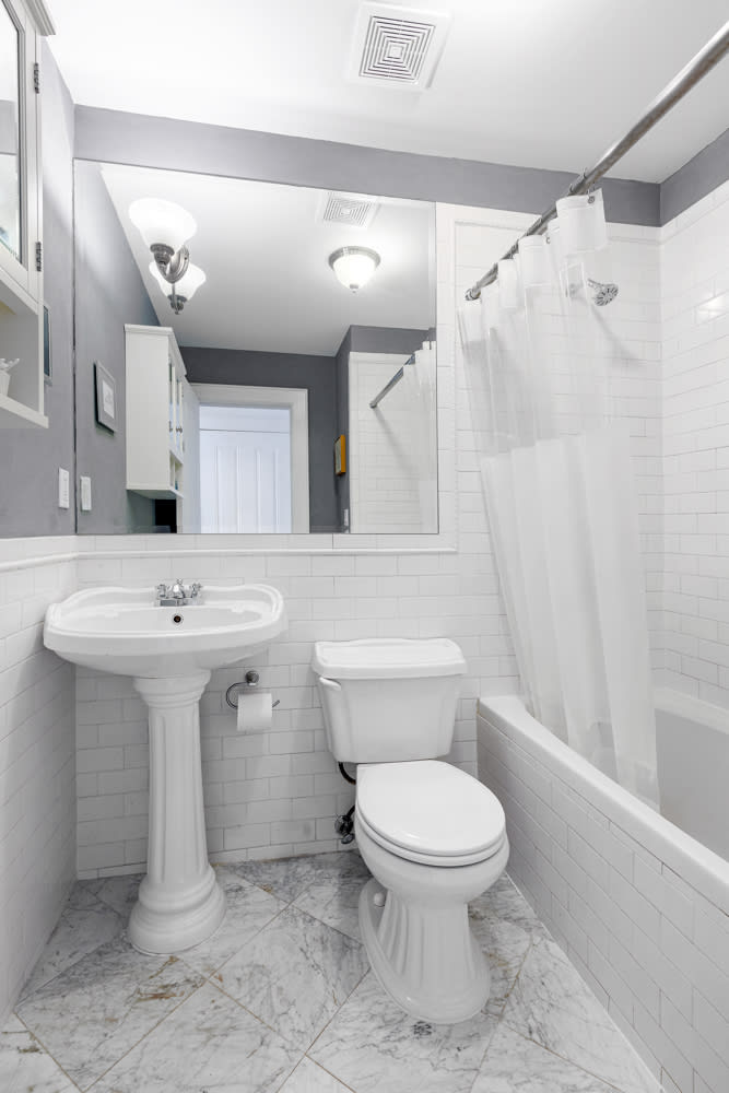 Bathroom with a pedestal sink, subway tile, and a tub behind a white shower curtain.