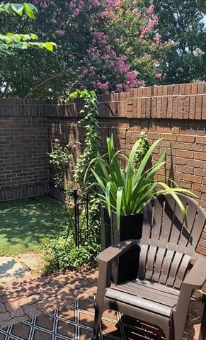 Private patio with a brown Adirondack chair, potted plants, and a brick privacy wall beneath a flowering tree.
