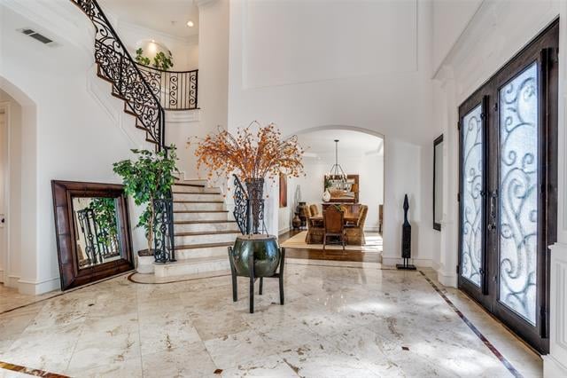 Furnished foyer with marble floors, an ornate staircase, and tall glass entry doors.