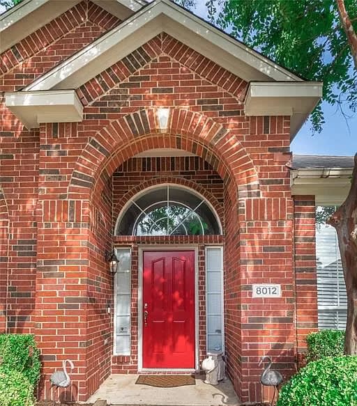 Red-brick home entrance with an arched portico and bright red front door.