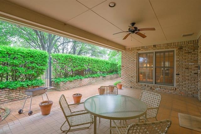 Covered brick patio with glass-top dining table, ceiling fan, and hedge-lined garden wall.