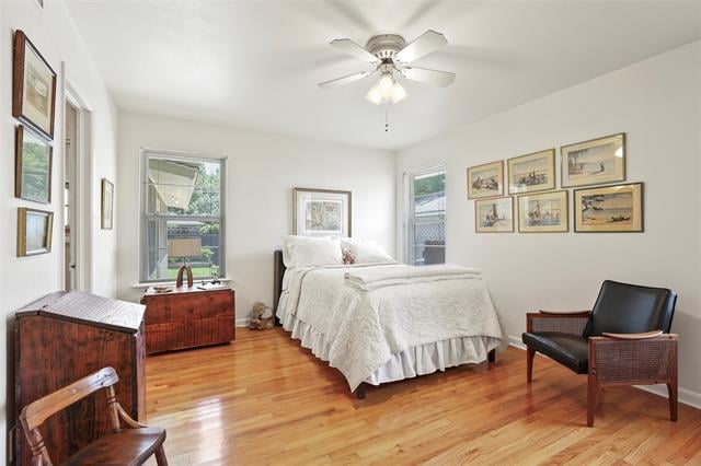 Bedroom with a white bed, polished hardwood floors, ceiling fan, and framed artwork.