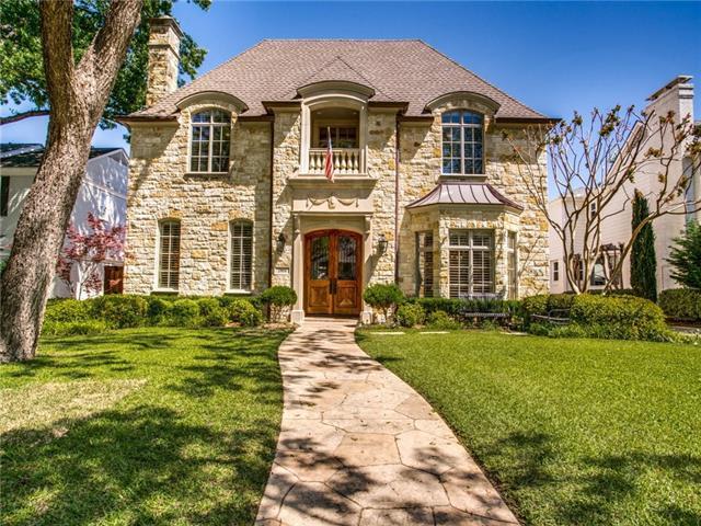 Two-story stone house with an arched entry, wooden double doors, and a curved walkway through the lawn.