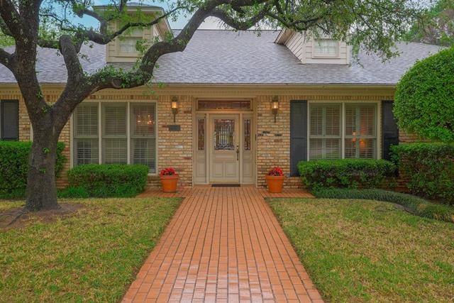 Brick home with dormer windows and a brick walkway leading to the front entry beneath a mature tree.
