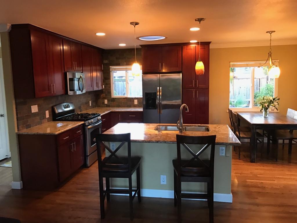 Kitchen with dark cherry cabinets, stainless steel appliances, and a stone-topped island with seating.