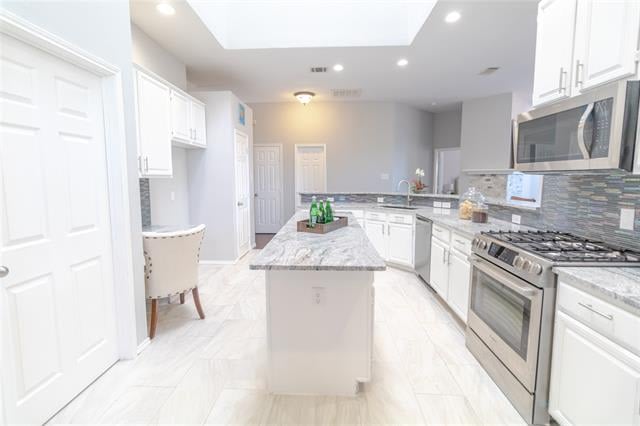 Bright white kitchen with a central island, gray tile backsplash, and stainless-steel range.