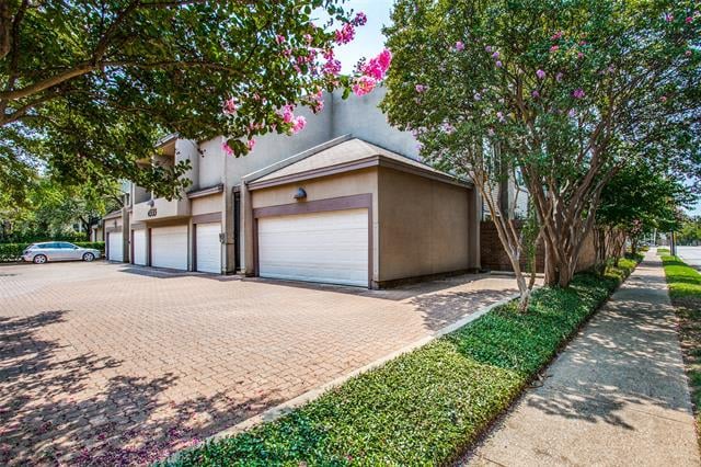 Residential building with white garage doors along a brick driveway beneath flowering trees.