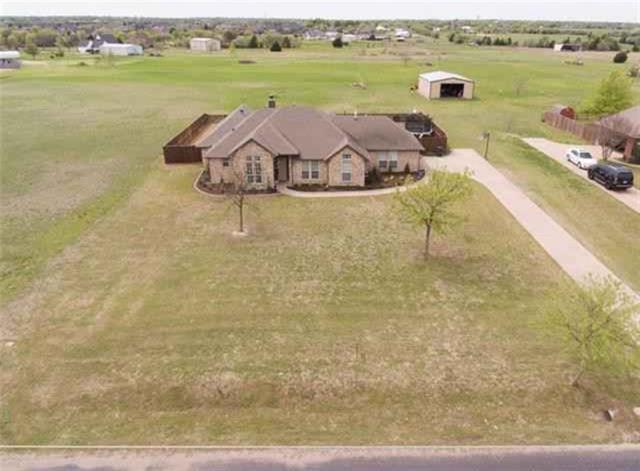 Aerial view of a brick home on a broad lot, with driveway and outbuildings.