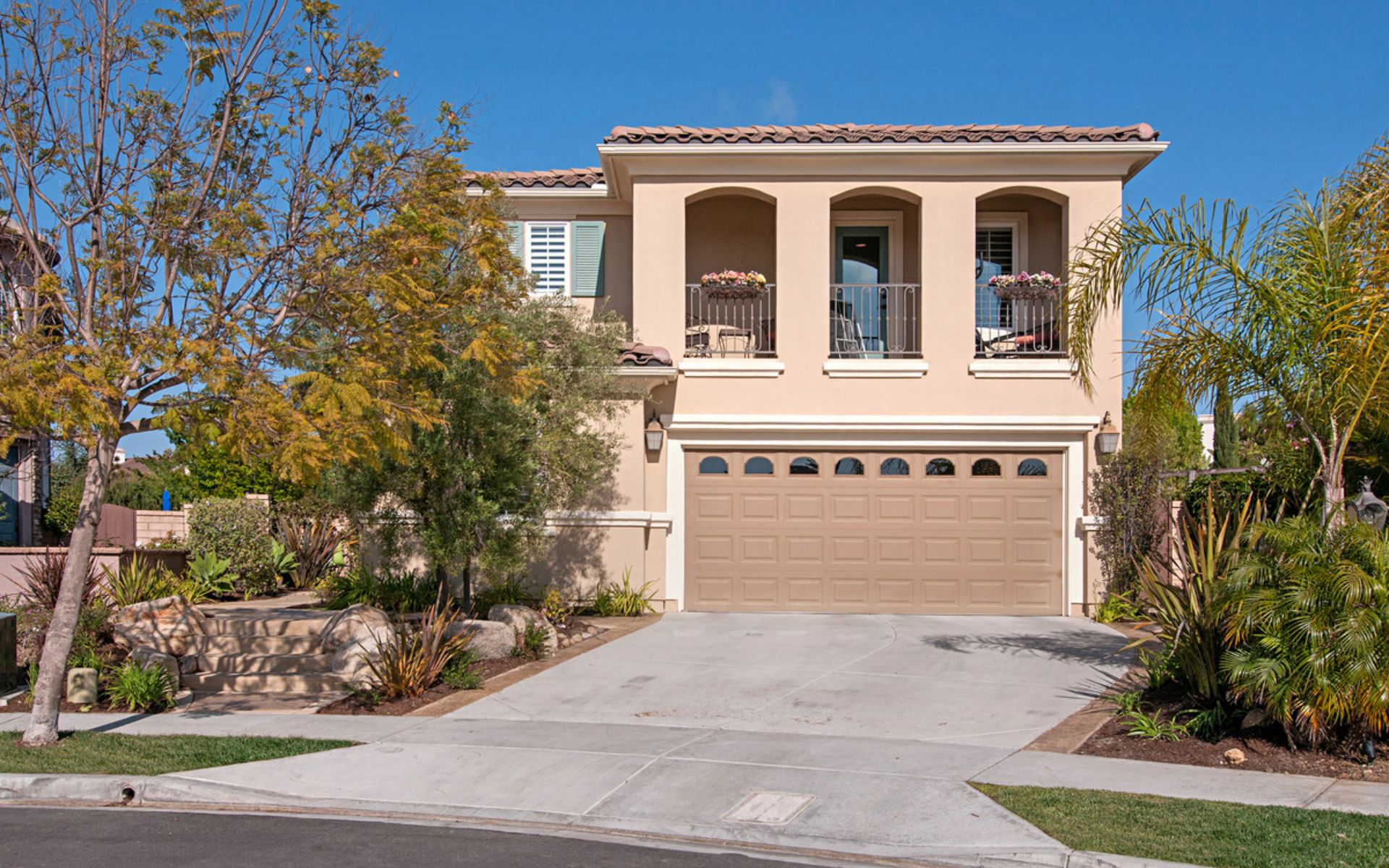 Two-story stucco home with arched balconies, a double garage, and landscaped front garden.