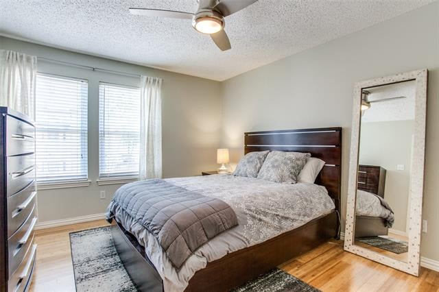 Bedroom with a dark wood platform bed, gray patterned bedding, and two windows with blinds.