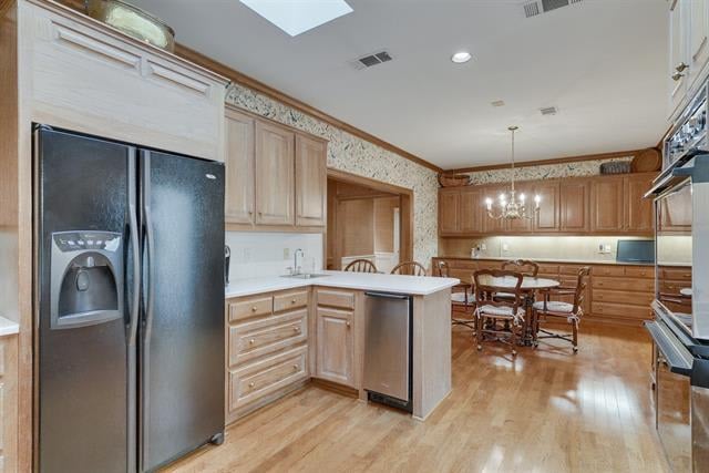 Kitchen with a central island, light wood cabinets, stainless steel appliances, and an adjoining dining area.