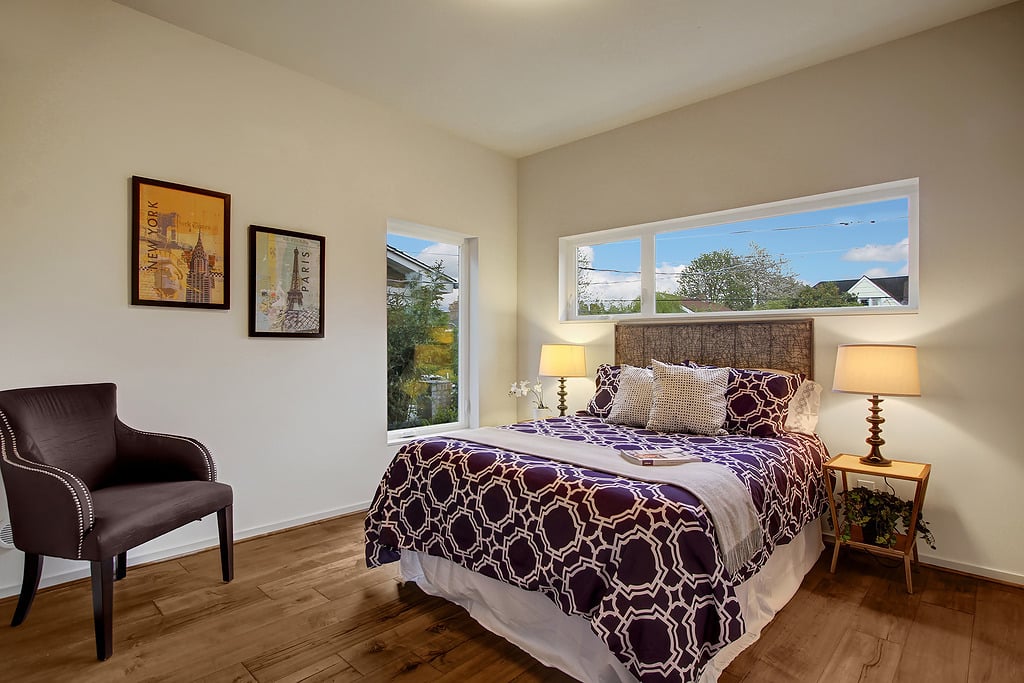 Staged bedroom with purple patterned bedding, a woven headboard, and wide windows overlooking the neighborhood.