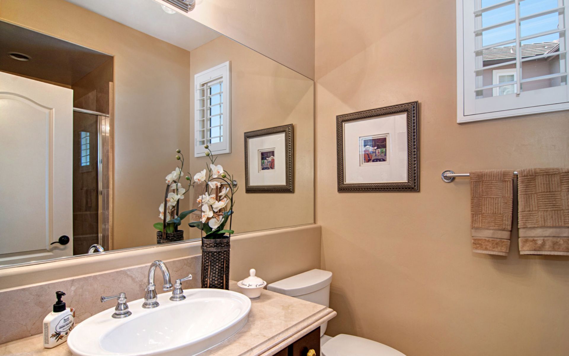 Bathroom with an oval sink, large mirror, orchids, and folded towels beside the toilet.