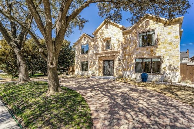 Two-story stone house with a paved driveway and mature trees in the front yard.