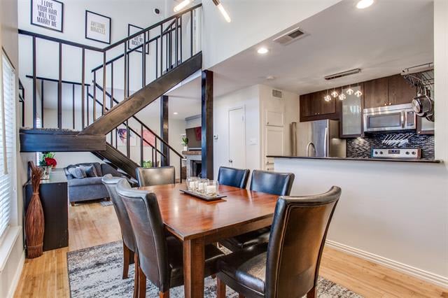 Dining area with a wooden table and leather chairs beside a modern kitchen and open staircase.