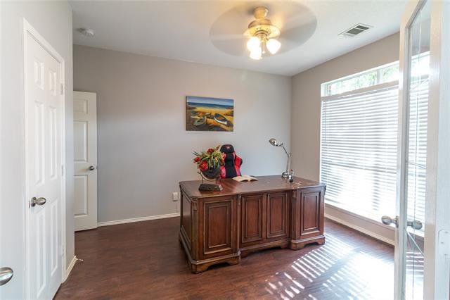 Home office with a large wooden desk and bright windows with blinds.