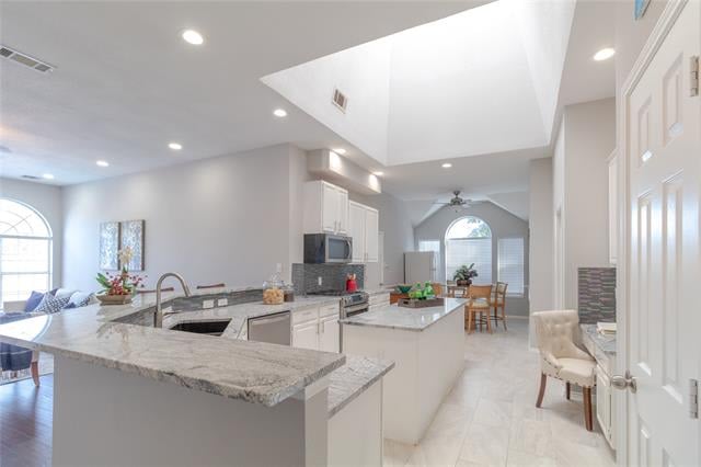 Open-plan kitchen with a granite island, white cabinets, and a large skylight.