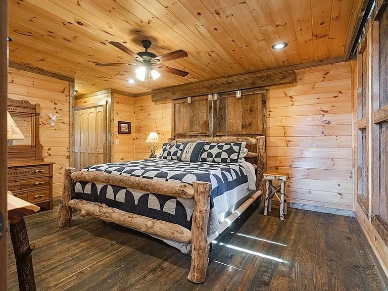 Rustic bedroom with a log-frame bed, black-and-white bedding, and knotty pine walls and ceiling.