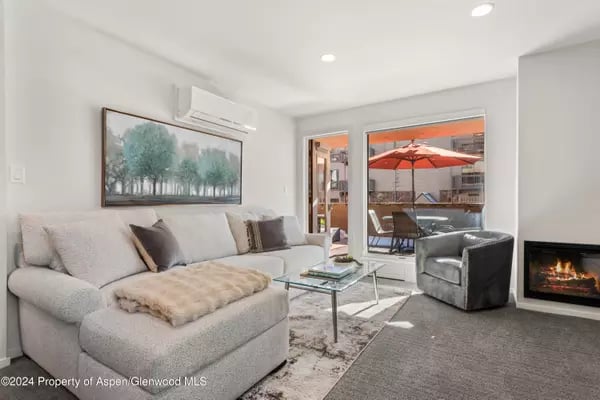 Living room with a pale sectional, glass coffee table, fireplace, and balcony with red umbrella.