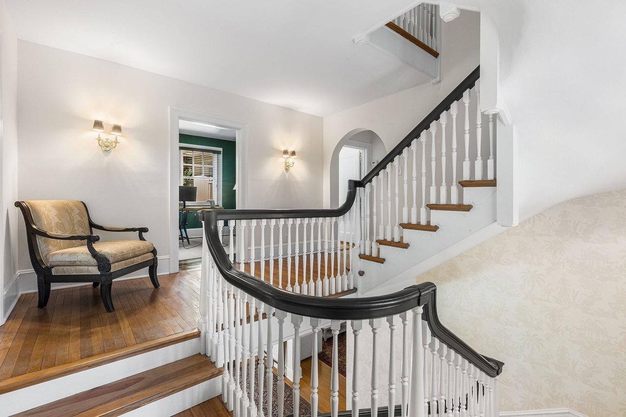 Foyer with a curved staircase, dark wood handrail, white balusters, and an upholstered chair on the landing.