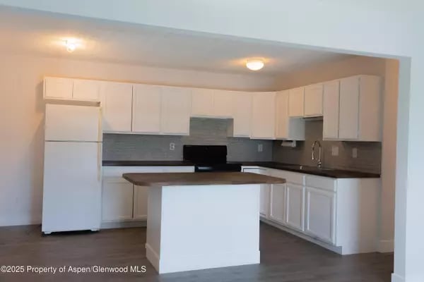 Kitchen with white cabinetry, gray tile backsplash, and a central island with a dark countertop.