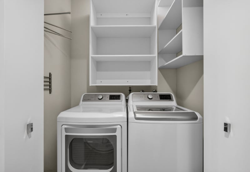 Laundry room with a front-loading dryer, top-loading washer, and built-in storage shelves.