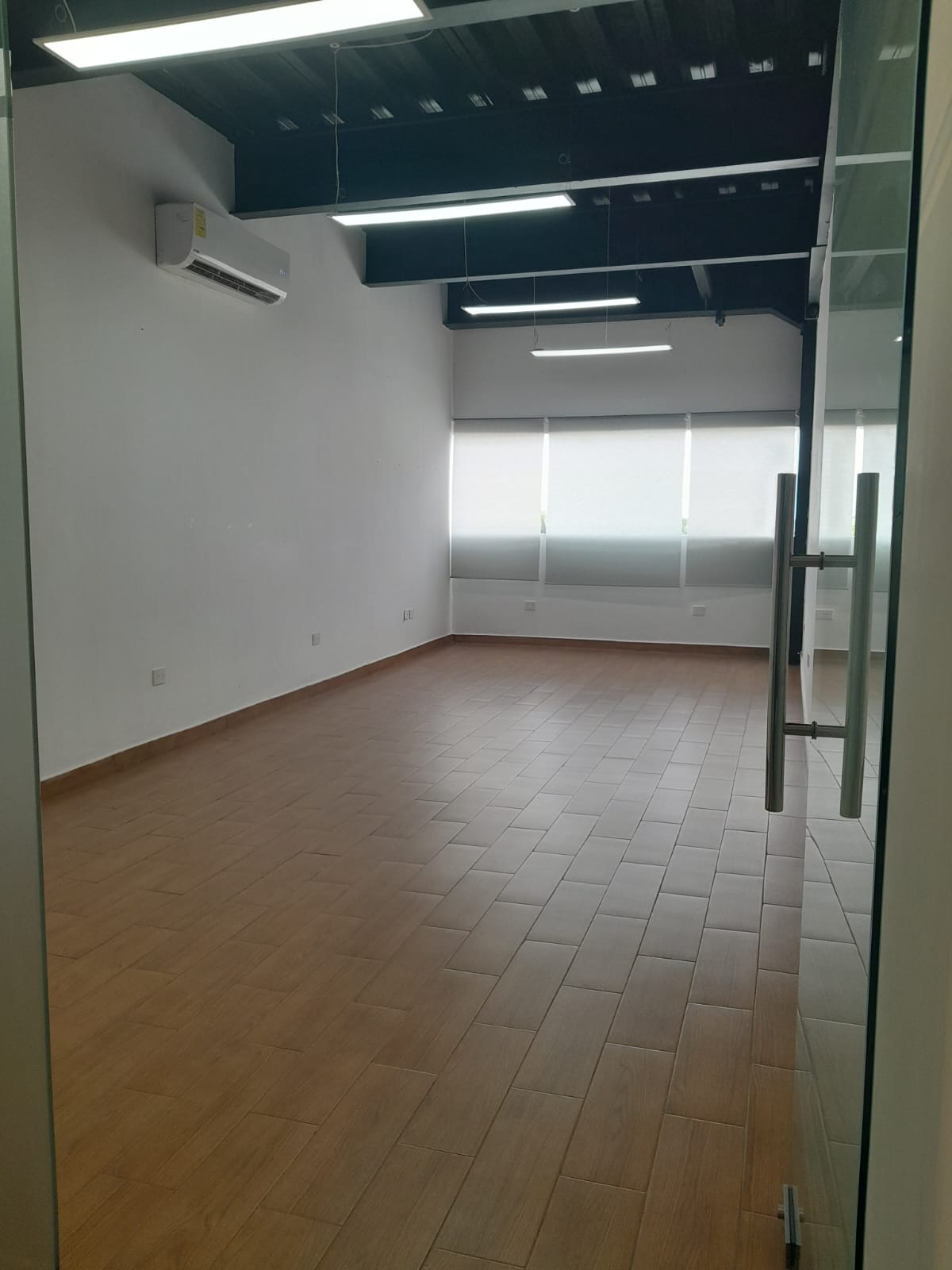 Vacant office with wood-look tile flooring, shaded windows, and exposed ceiling beams.