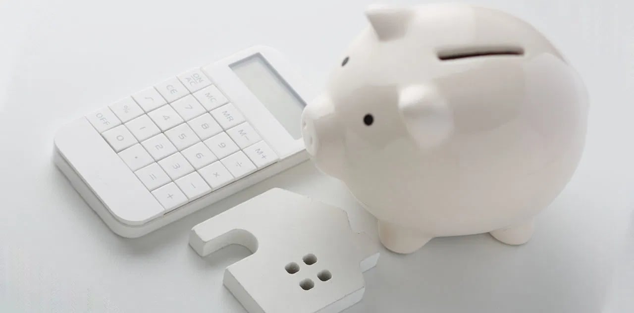 A white piggy bank beside a calculator and a house-shaped savings token.