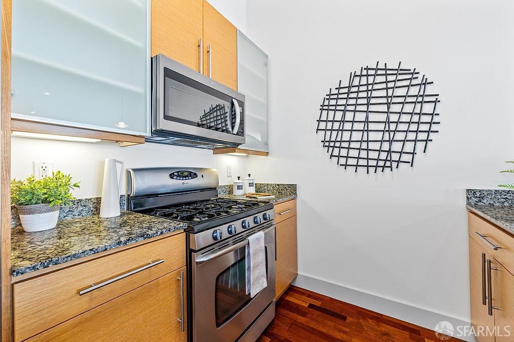 Kitchen with light wood cabinets, granite counters, stainless steel appliances, and a black metal wall sculpture.