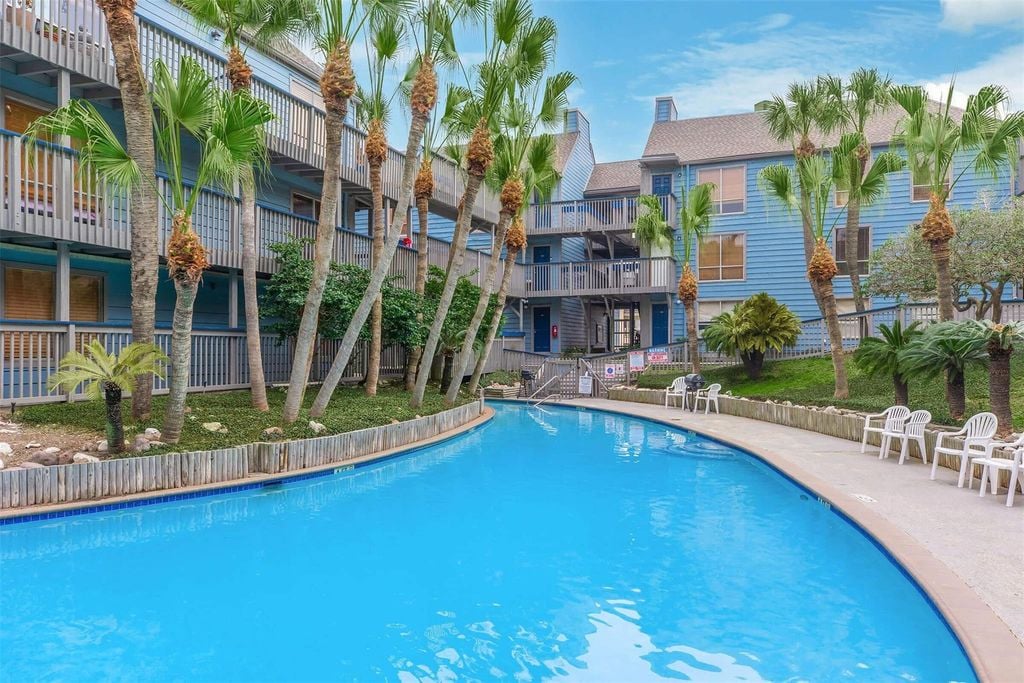 Swimming pool beside blue condominium buildings and palm-lined balconies.