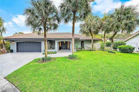 Single-story home with an attached garage, palm trees, and a broad green lawn.