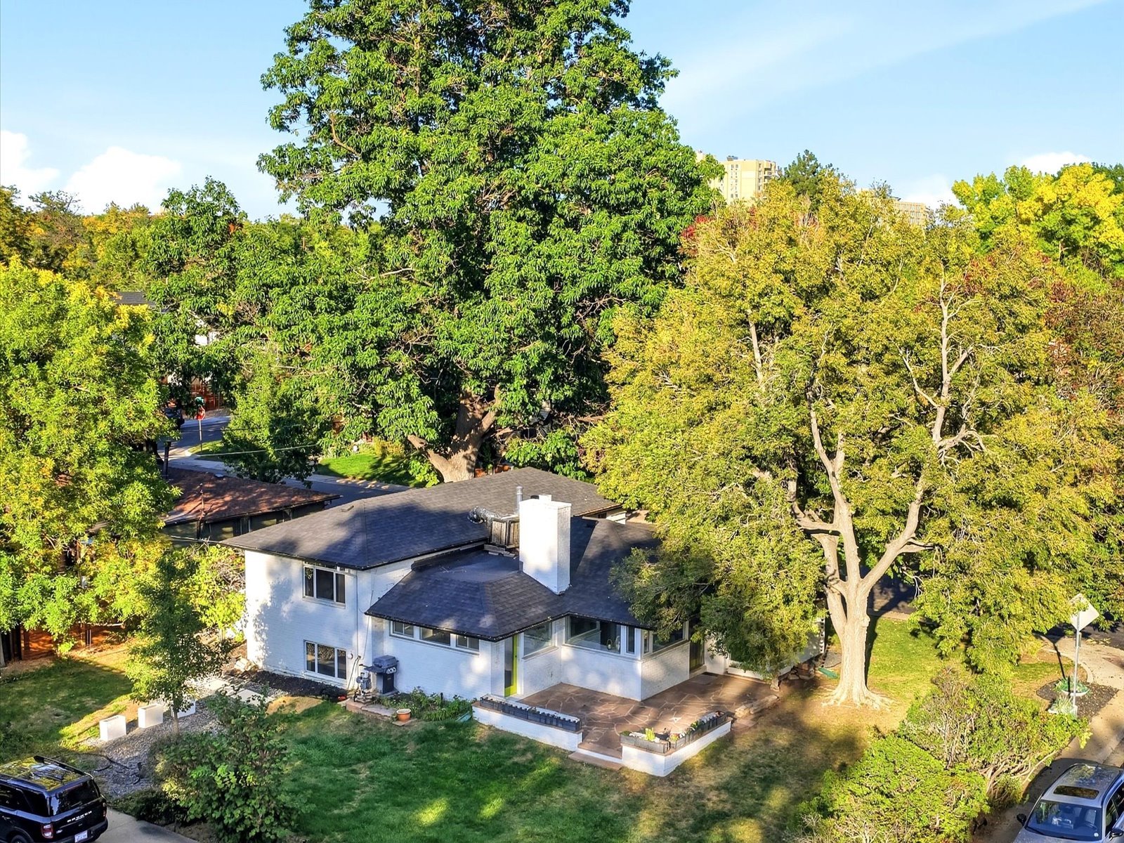 Aerial view of a white mid-century home with a dark roof, patio, and mature trees.